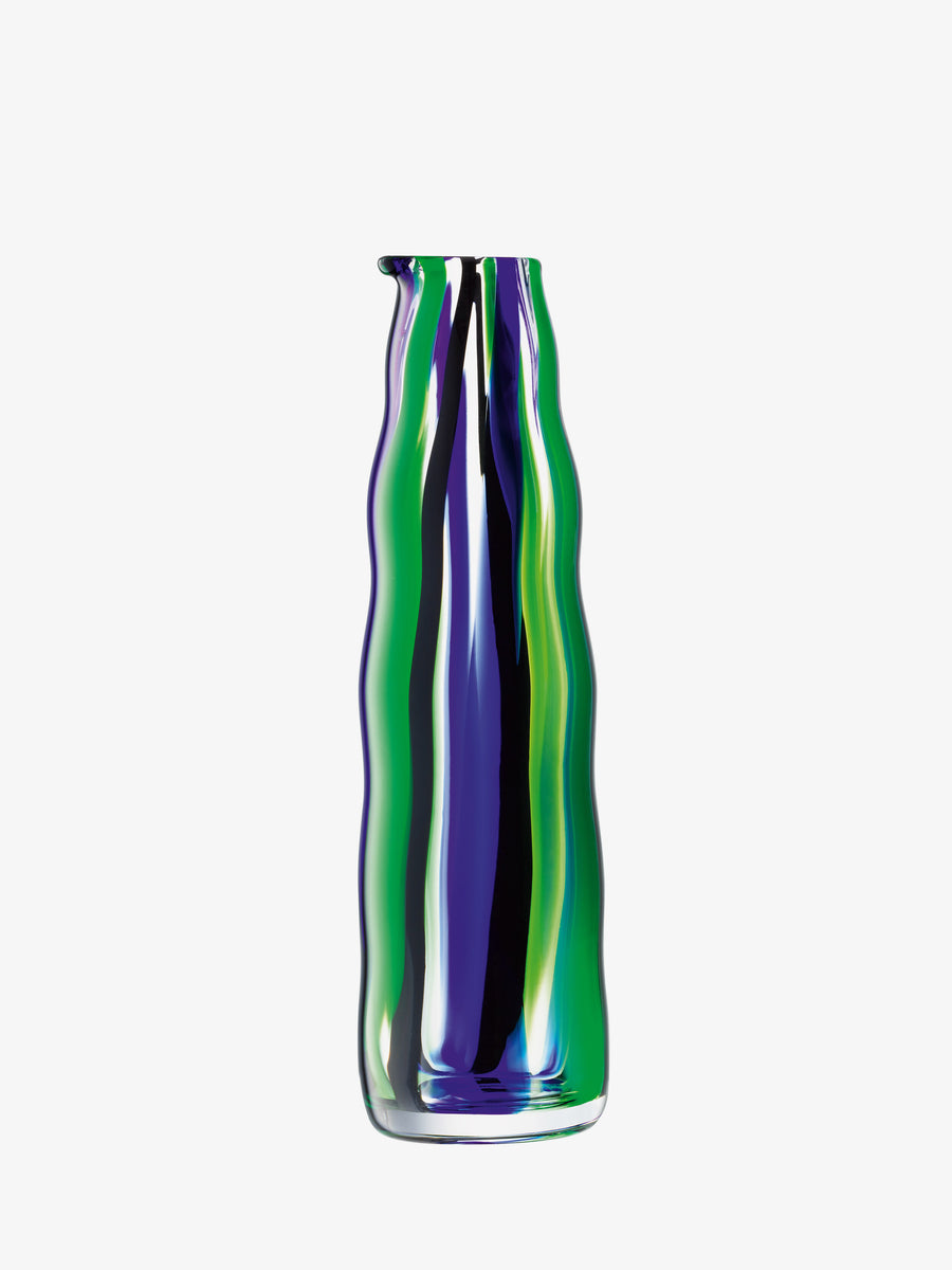 Carafe by lsa-international with tall, wavy-sided glass design, showcasing iridescent blue, green, and yellow vertical stripes in a folk-inspired pattern, presented against a plain white background.