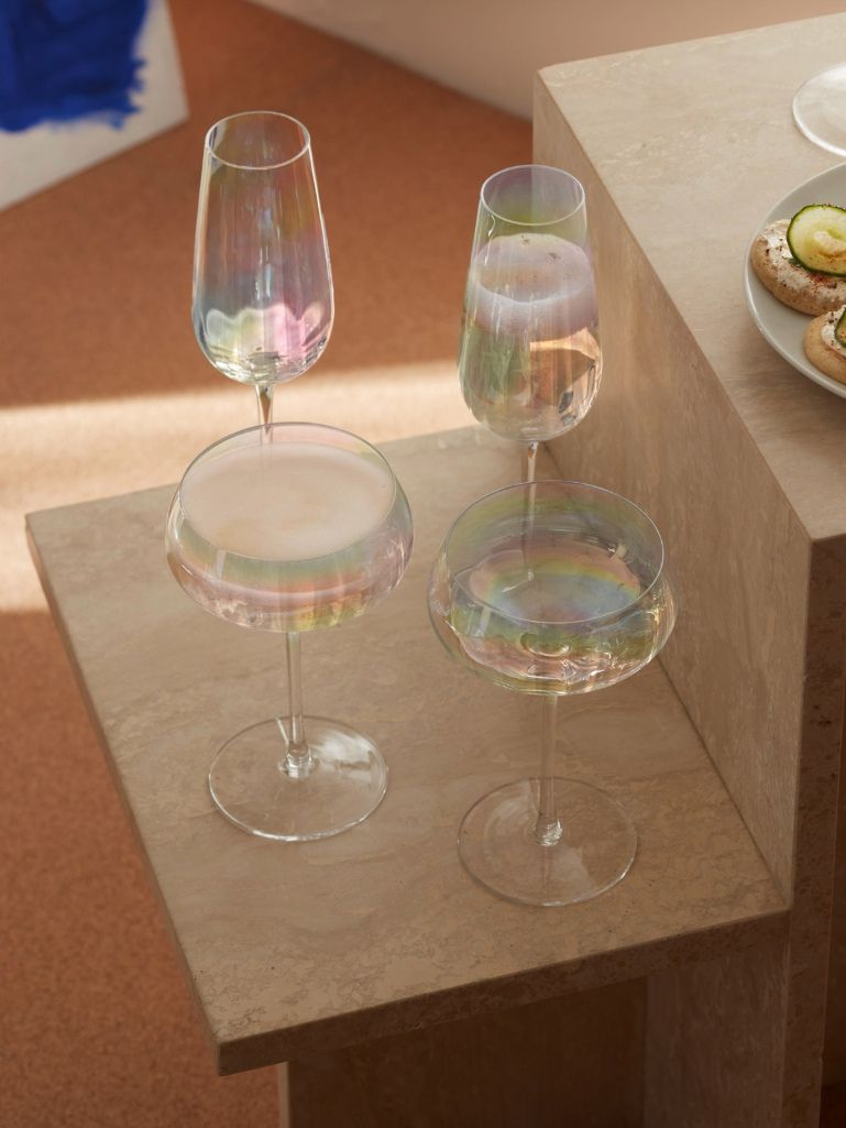 Four iridescent clear glass wine glasses arranged on a beige stone pedestal in a warm indoor setting.