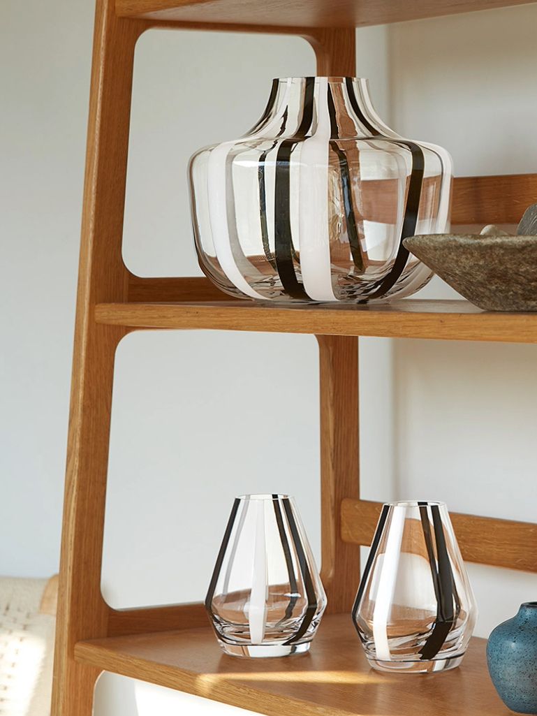 A set of clear glass vases with bold black vertical stripes, displayed on wooden shelves against a light wall.