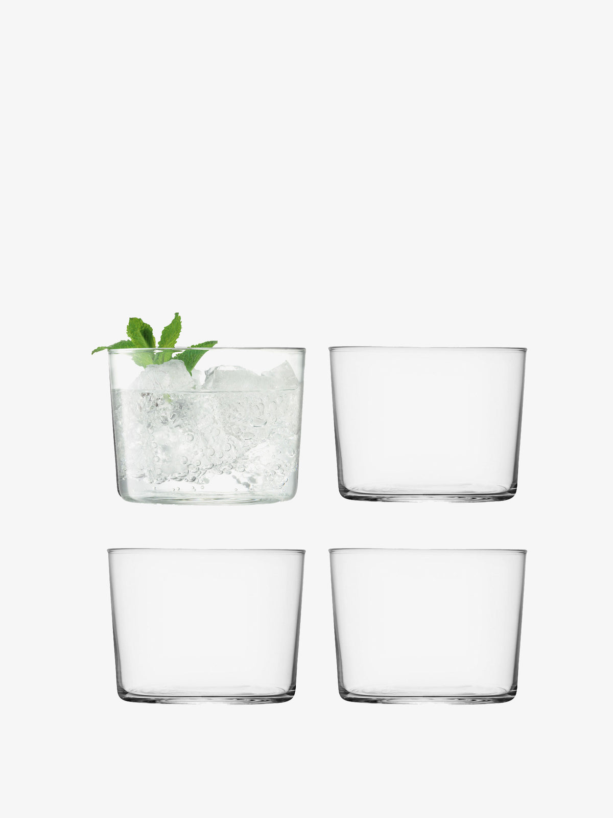 Four lsa-international Tumbler glasses are arranged in a grid. The top left glass contains ice and a sprig of mint, while the other three are empty. Crafted from clear, versatile glass, these stackable Tumbler glasses sit against a plain white background.