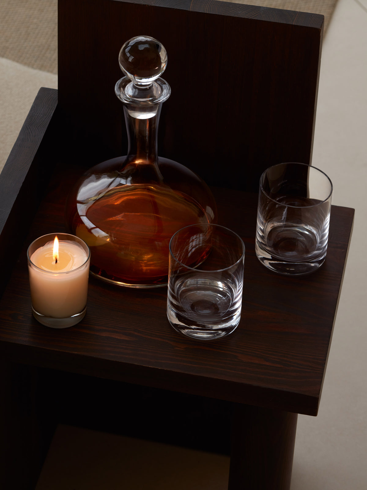 A lsa-international Tumbler, paired with a glass decanter filled with amber liquid and a lit candle, sits on a dark wooden side table.