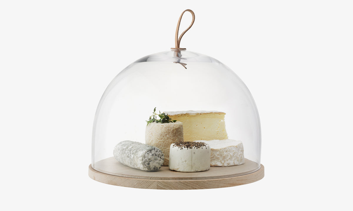 A selection of various cheeses on an lsa-international Dome & Ash Base, covered by a clear glass dome with a leather handle.