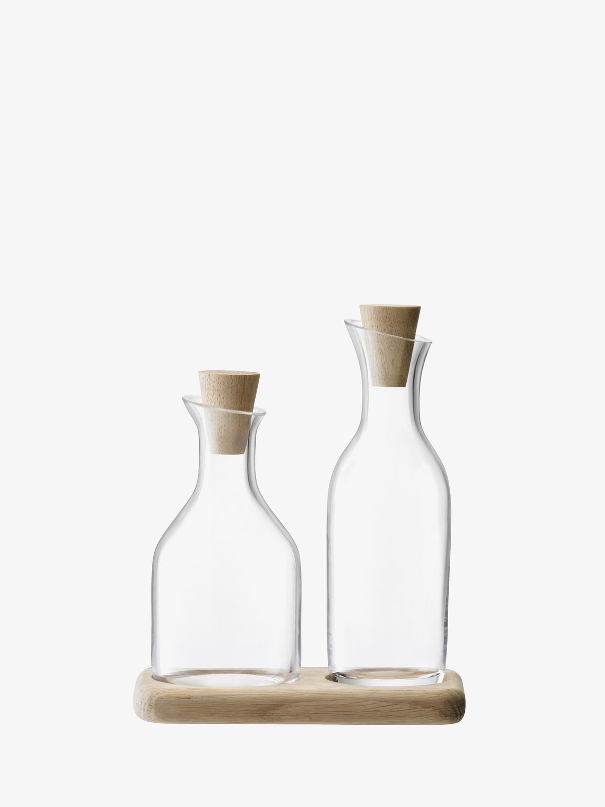 The Oil & Vinegar Set & Oak Base by lsa-international features two clear mouth-blown glass bottles—one shorter and wider, the other taller and slimmer—each topped with an oak stopper, neatly displayed on a light wooden tray against a white background.