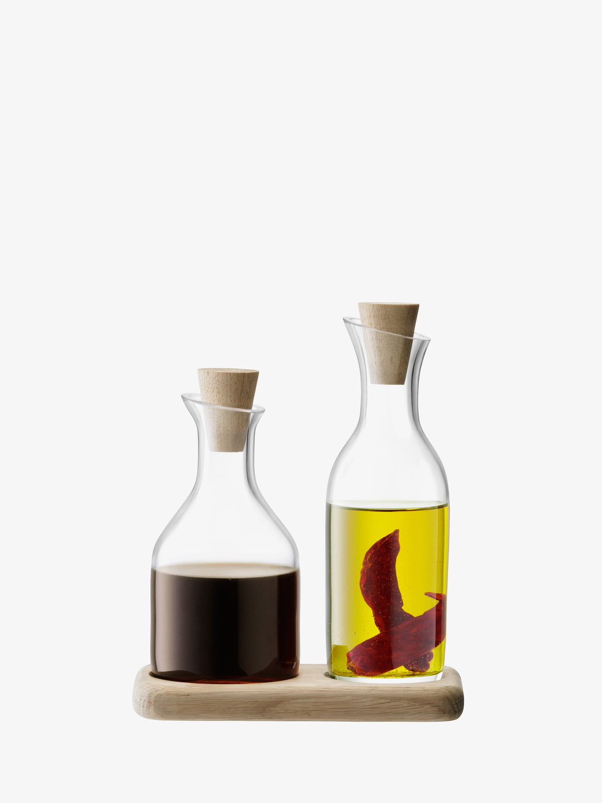 The lsa-international Oil & Vinegar Set & Oak Base features two mouth-blown glass bottles, each topped with an elegant oak stopper, neatly arranged on a compact wooden tray. One bottle holds rich vinegar and the other contains golden oil infused with red chili slices, both displayed against a plain white background.