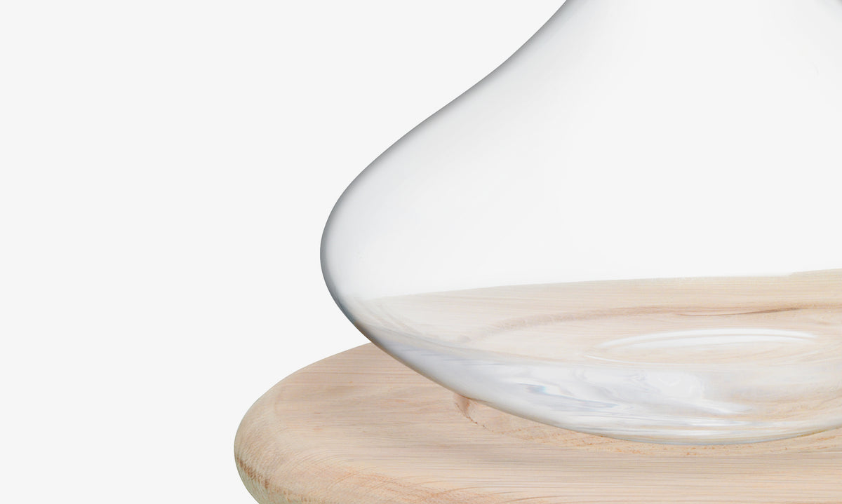 A close-up of the lsa-international Carafe & Oak Cheese Board, featuring a clear glass carafe resting on a round oak board against a white background, emphasizing its elegant simplicity and wine aeration potential.