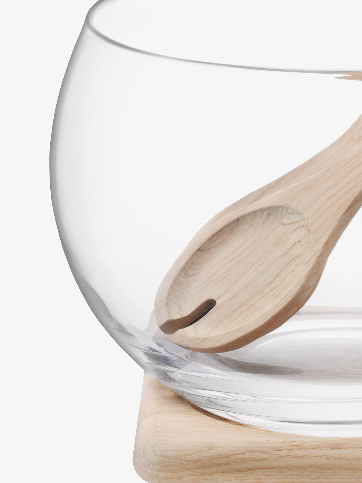 A close-up of the lsa-international Salad Set & Oak Base, featuring a mouth-blown glass bowl with a wooden spoon nestled inside, displayed on its light oak base against a white background.