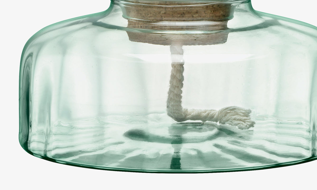 Close-up of the lower part of an lsa-international Self Watering Planter Clear/Part Optic, featuring transparent recycled glass with a white braided wick inside and a cork stopper at the top, reminiscent of an oil lamp.