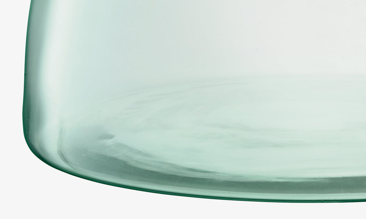 Close-up of the base of the lsa-international Closed Garden planter in transparent light green recycled glass, highlighting its smooth curves and subtle reflections.