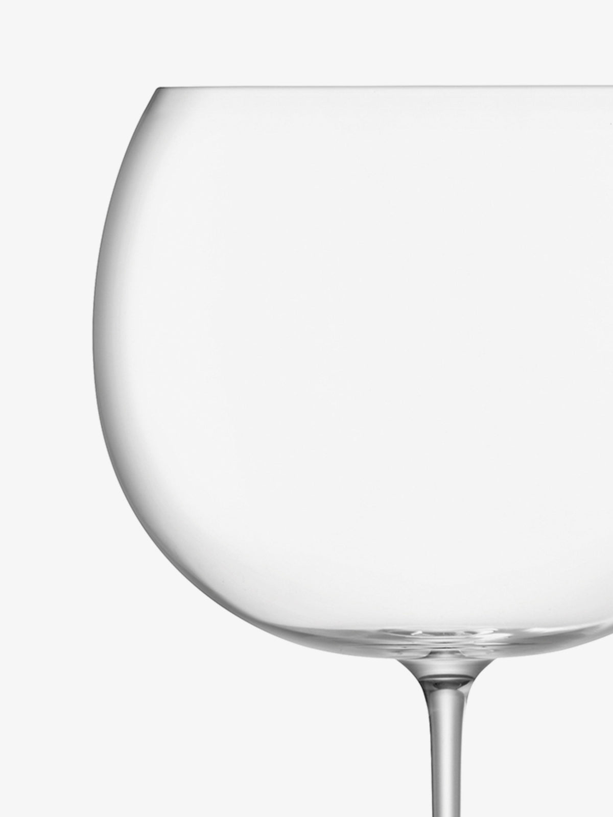 A close-up of a large, empty, clear wine glass with a thin stem against a plain white background.