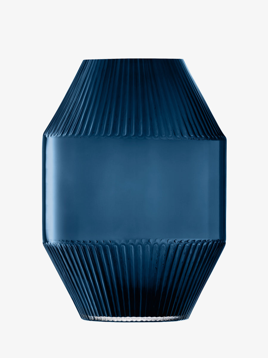 The lsa-international Vase features a sapphire blue glass construction with a geometric silhouette. Its design showcases ribbed textures at the top and bottom, contrasted by a smooth, wide middle section—drawing inspiration from the sleek lines of contemporary architecture. This mouth-blown vase from lsa-international stands out beautifully against a plain white background.