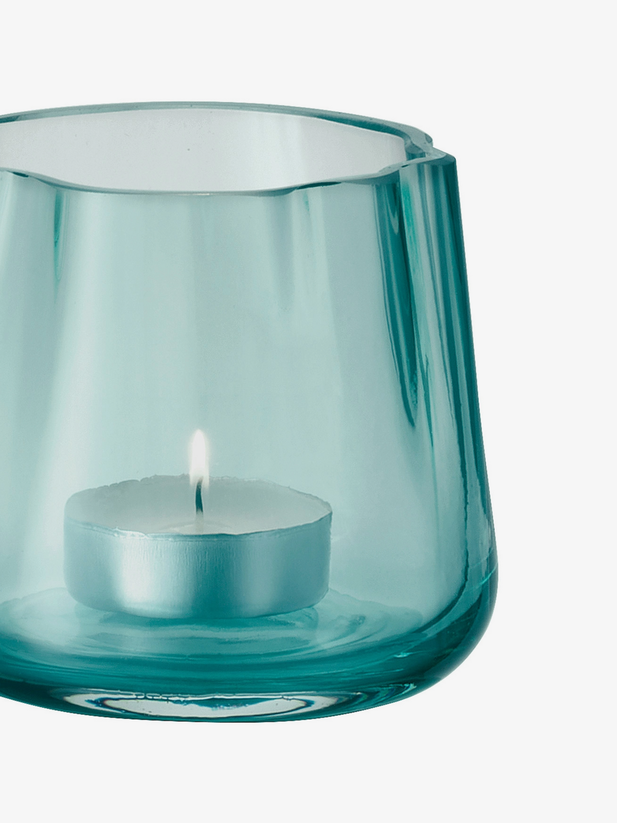 A small tealight candle is burning inside a round, transparent blue glass holder against a white background.