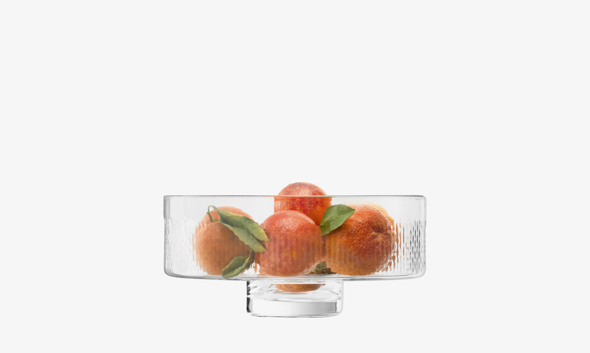 The lsa-international Comport, featuring a clear textured surface and an elegant pillar stem, holds several oranges with green leaves and is set against a plain white background.