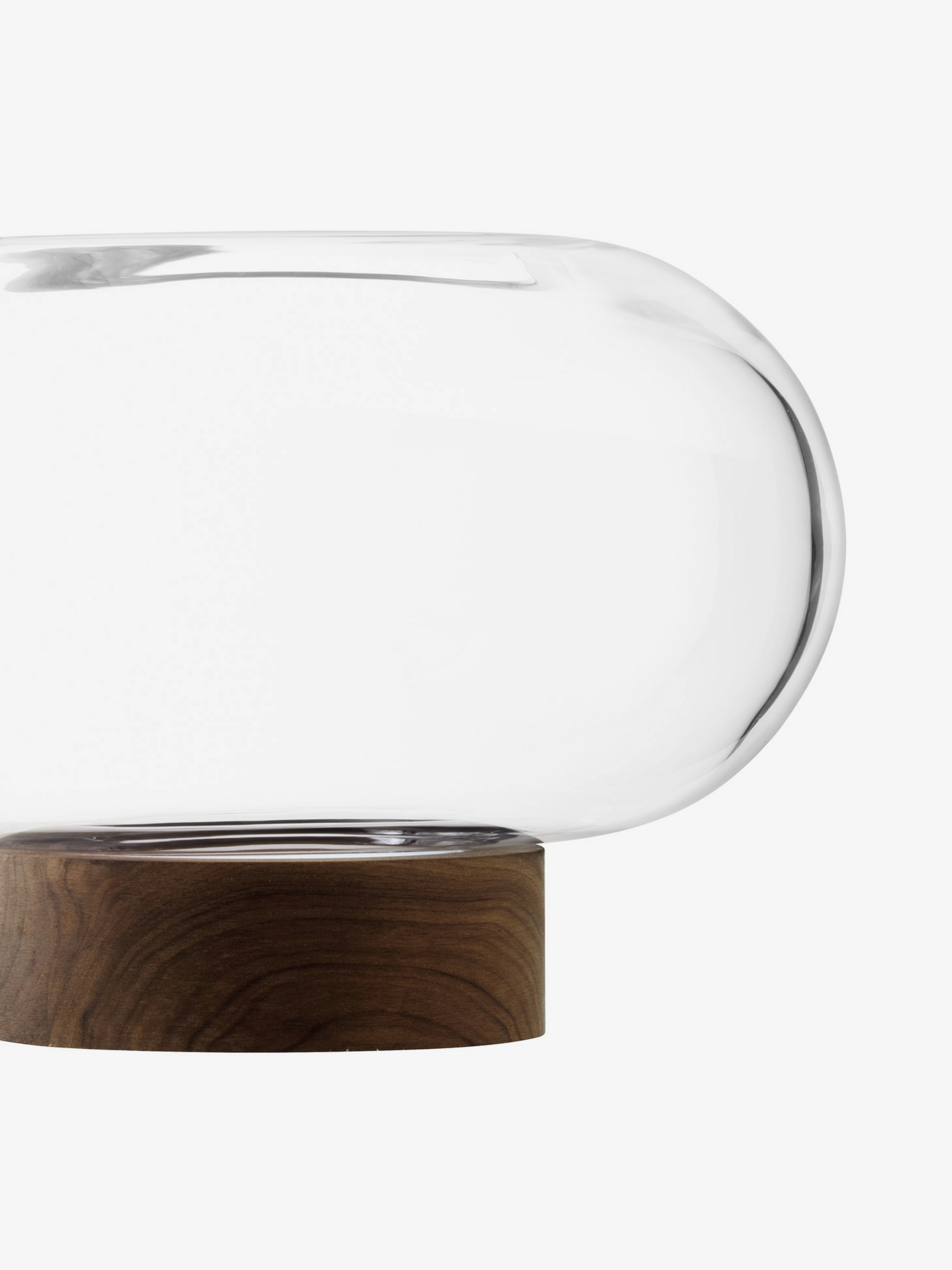 A clear, rounded glass bowl with an elongated shape sits atop a circular wooden base, photographed on a white background.