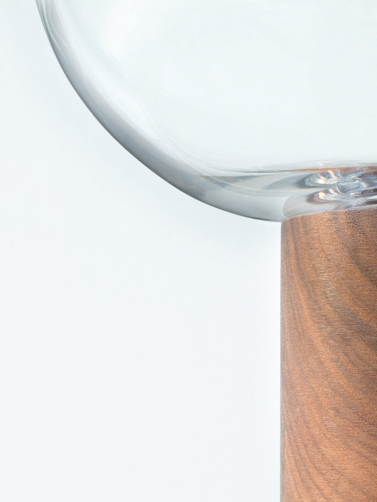 An LSA International vase featuring a mouth-blown glass bowl resting on a cylindrical walnut base.