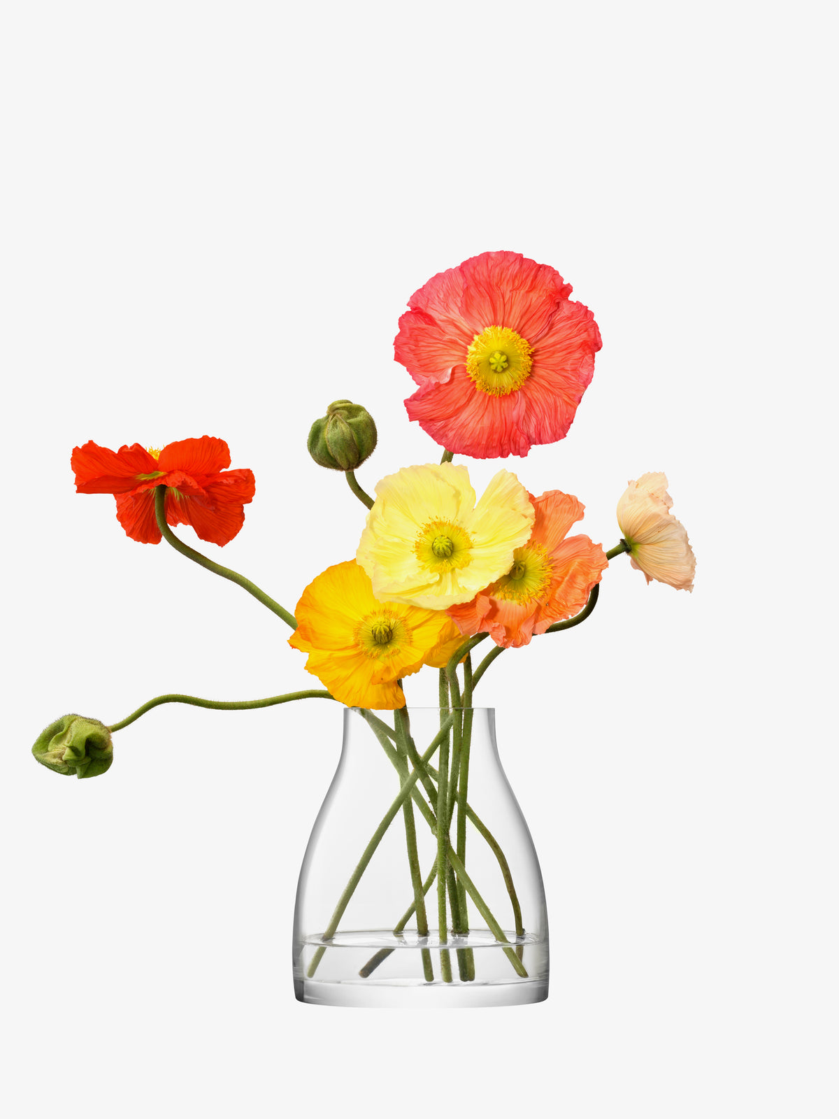 The Kiln Vase by lsa-international, crafted from mouth-blown glass, holds seven vibrant poppy flowers with yellow, orange, pink, and red petals on long green stems, arranged against a plain white background.