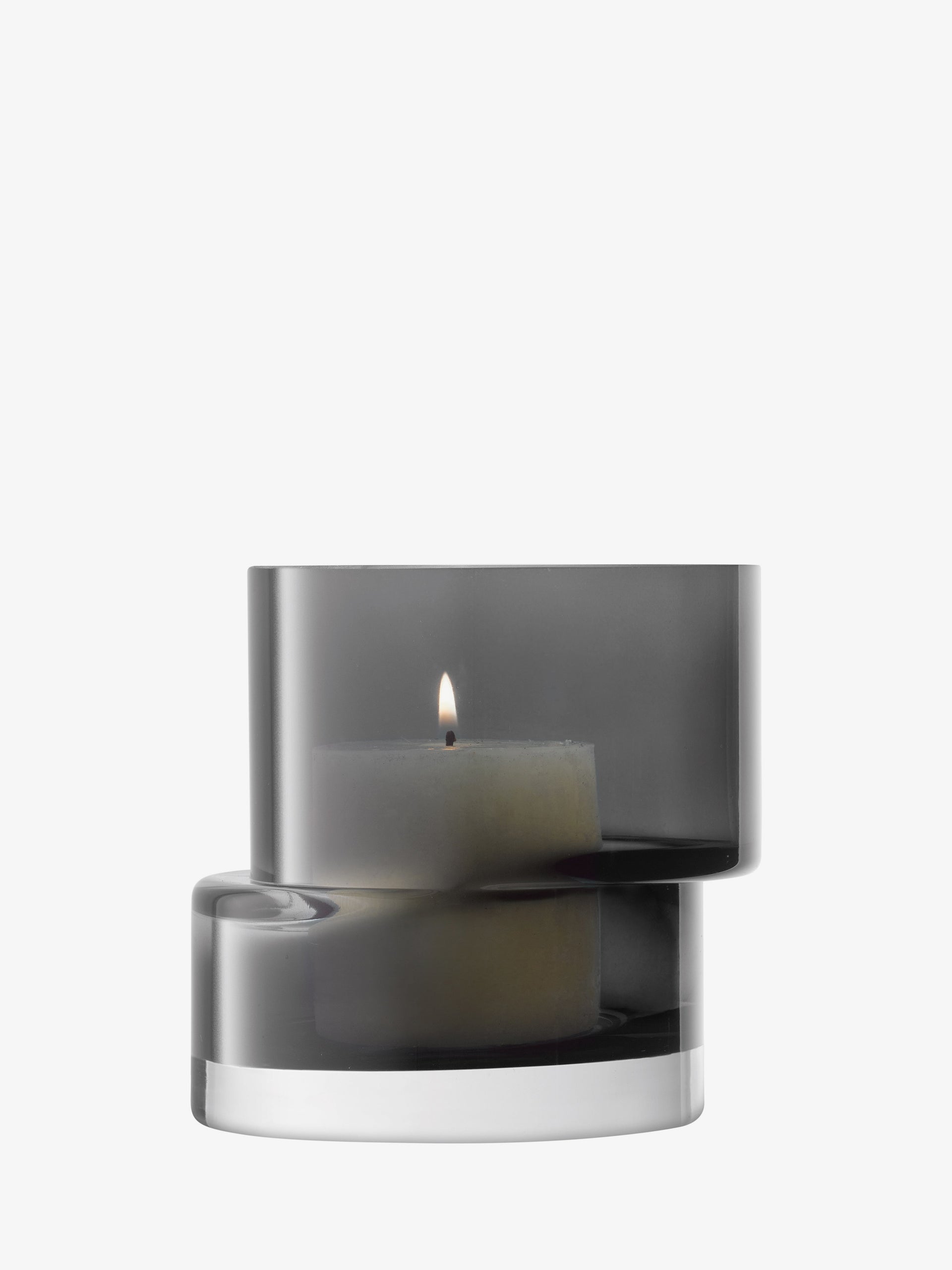 A small, lit pillar candle rests in the lsa-international Lantern/Vase—a modern, double-layered glass holder with a smoky gray finish—set against a plain white background and evoking the style of a geometric vase or mouth-blown lantern.