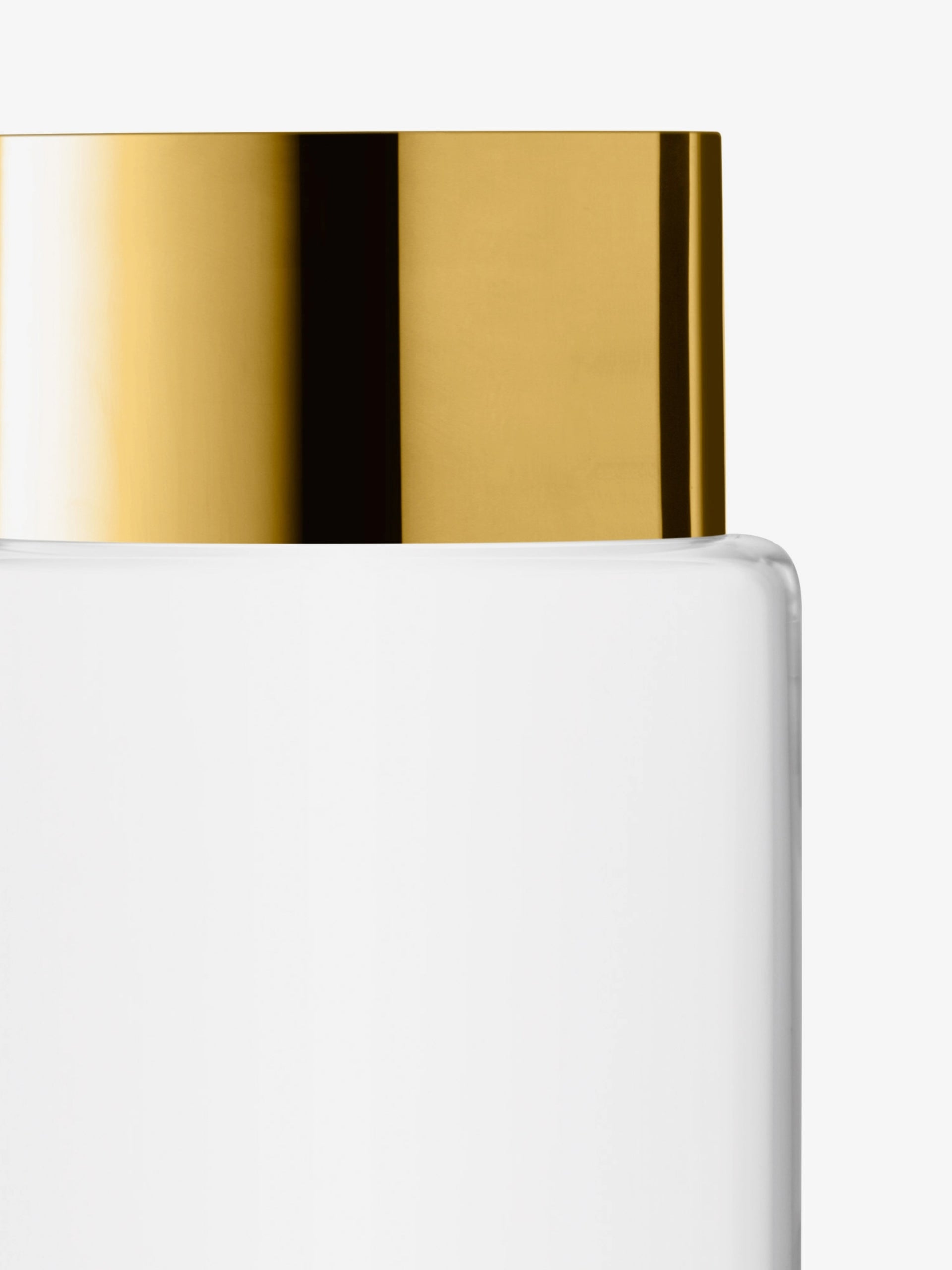 A close-up of a clear glass container with a shiny gold-colored metal lid, set against a plain white background.