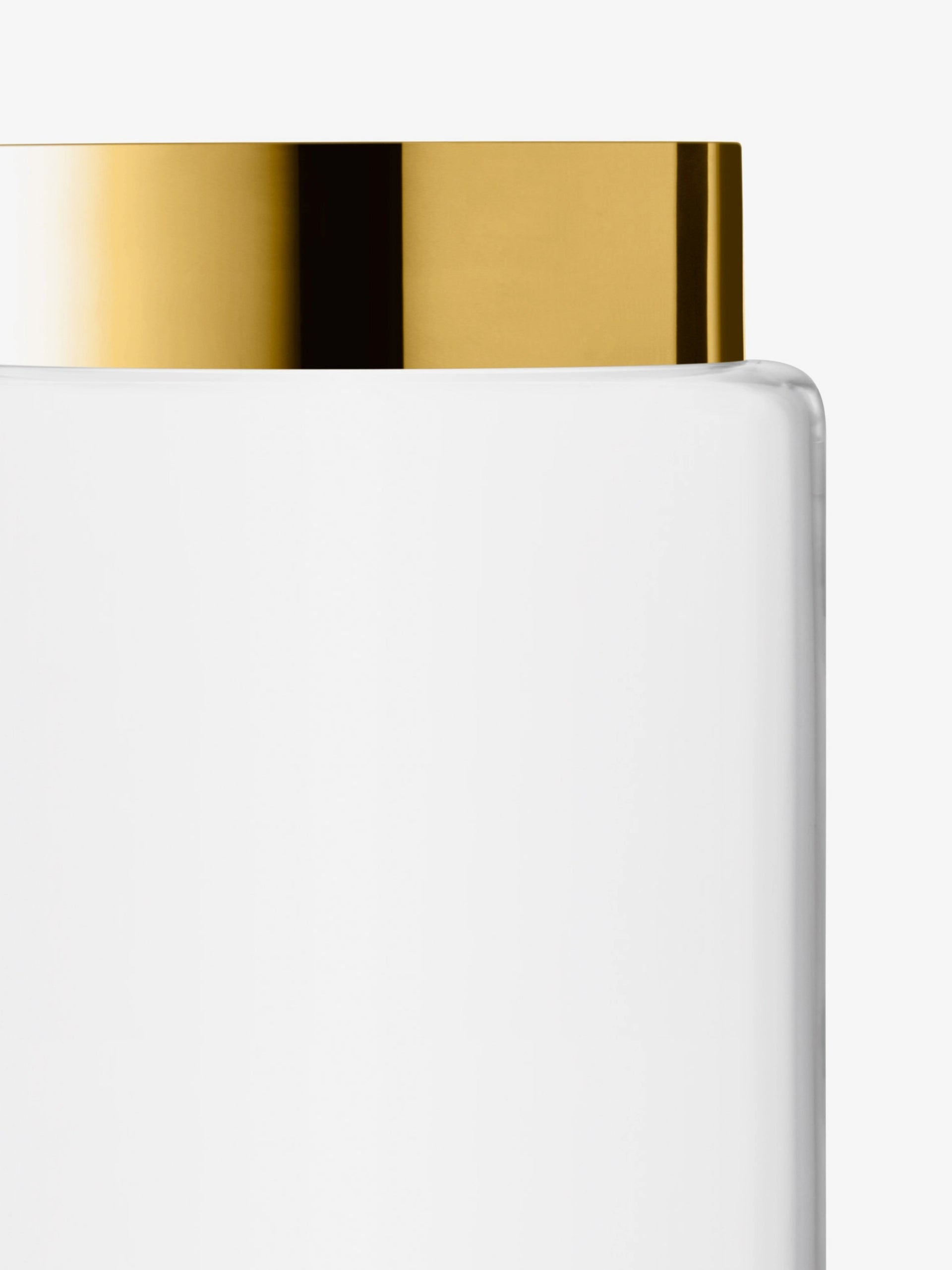 A close-up of a clear glass container with a shiny gold lid, photographed against a plain white background.