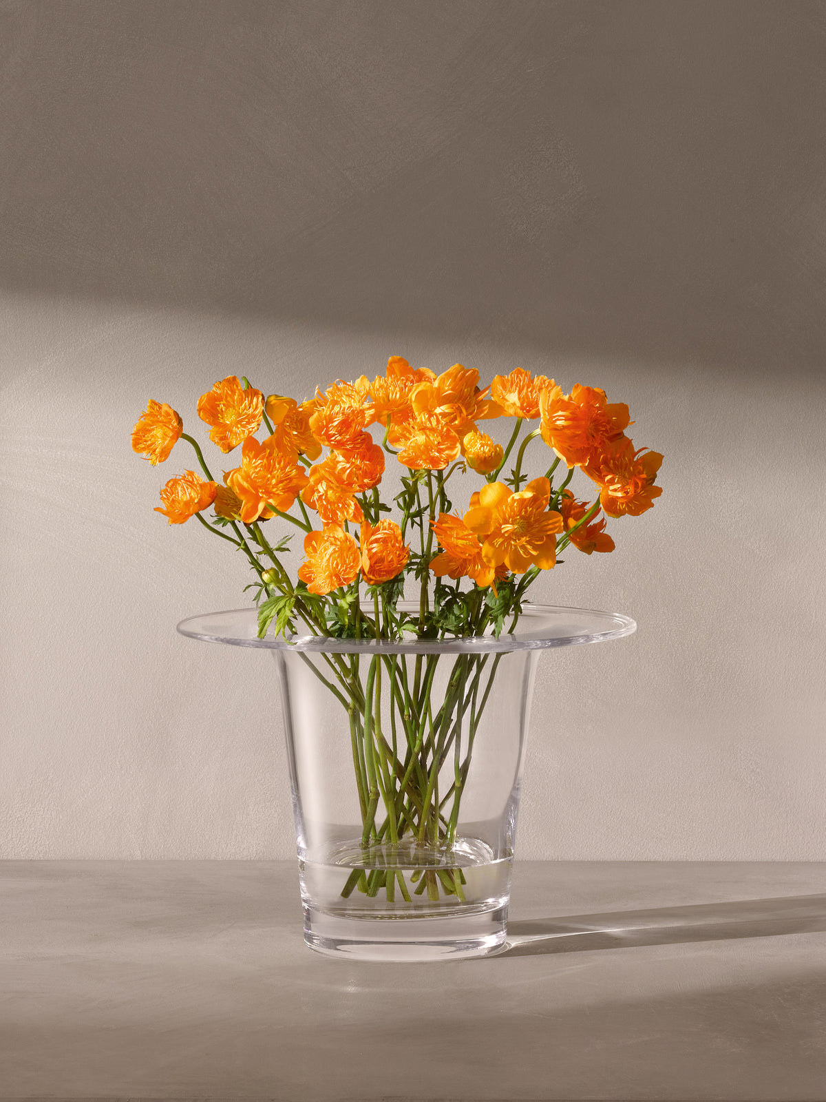A bouquet of bright orange globe flowers in a clear, mouth-blown LSA International Vase/Lantern with a wide rim.
