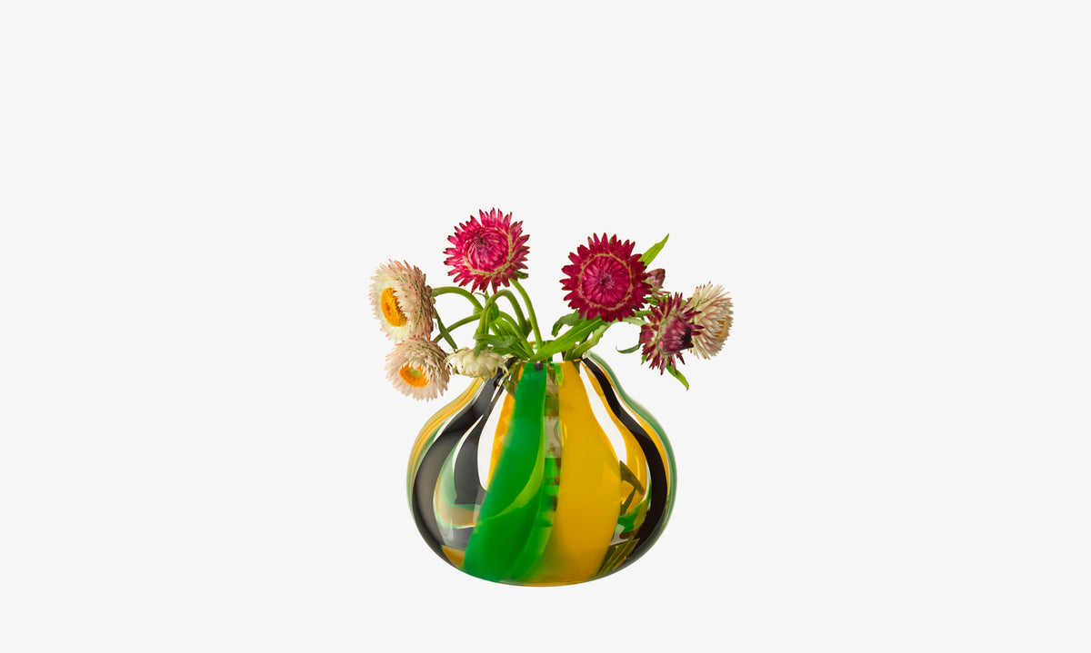 The lsa-international Vase, a round mouth-blown piece with green, yellow, and brown swirls, is filled with pink, yellow, and white dried strawflowers against a plain white background.