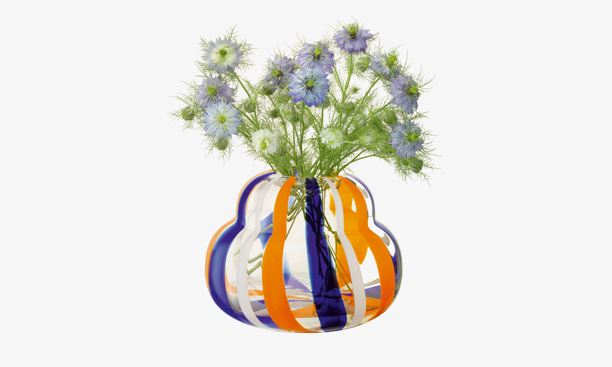 The lsa-international Vase with blue, orange, and white stripes displays light purple flowers and green feathery leaves against a white background.