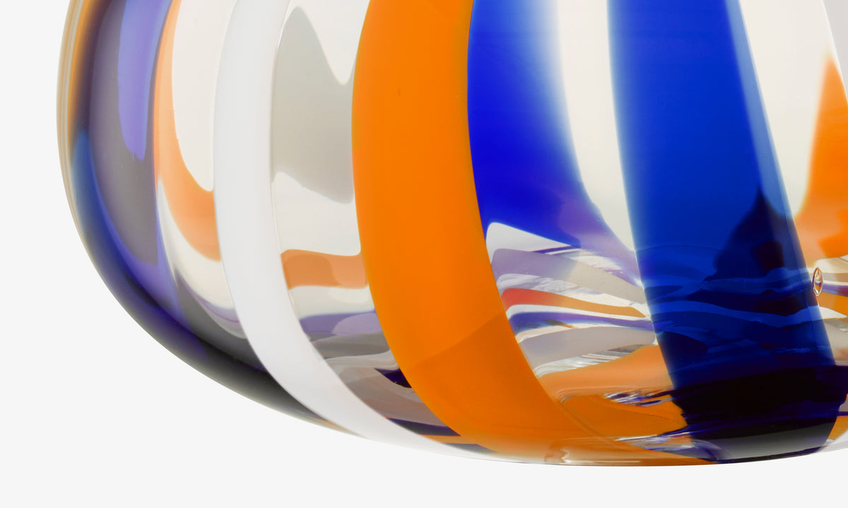 Close-up of the lsa-international Vase featuring bold blue, orange, and white vertical stripes on a clear surface, creating a visually striking and colorful abstract pattern.