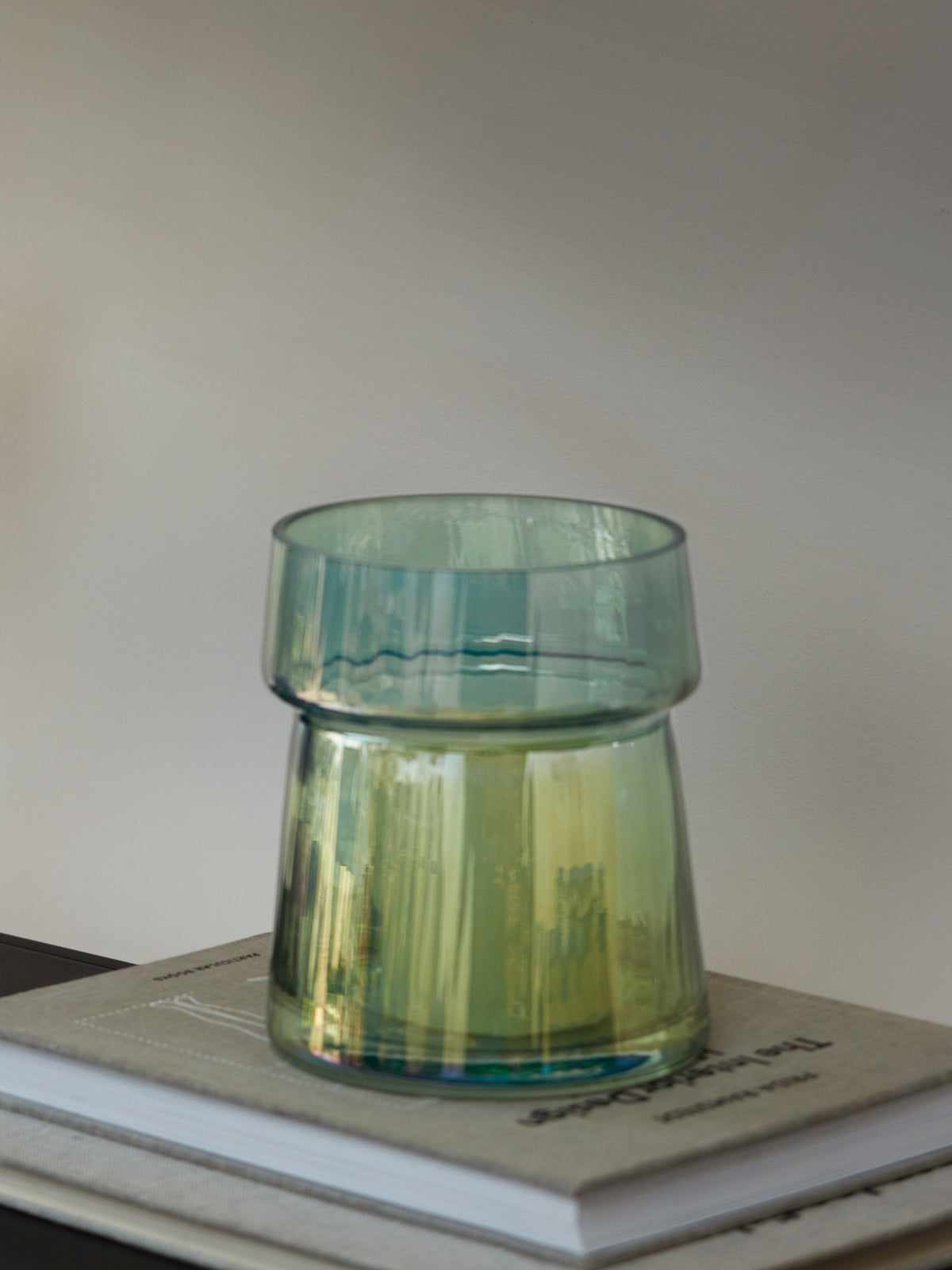 A translucent green Vase/Lantern by lsa-international, mouth-blown with a subtle pleated texture, sits atop two stacked books with beige and white covers against a neutral background.