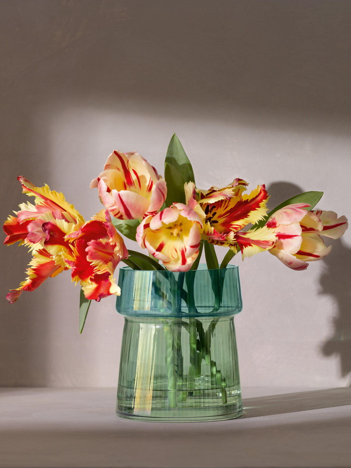 An lsa-international Vase/Lantern with a mouth-blown, pleated glass design holds a bouquet of yellow and red parrot tulips with jagged petals, set against a neutral background with soft lighting and gentle shadows.