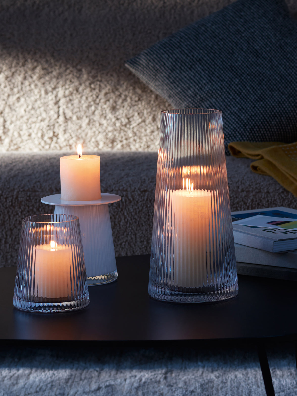 Three LSA International Lantern/Vase pieces in varying heights contain glowing pillar candles, creating ambient light on a dark coffee table.