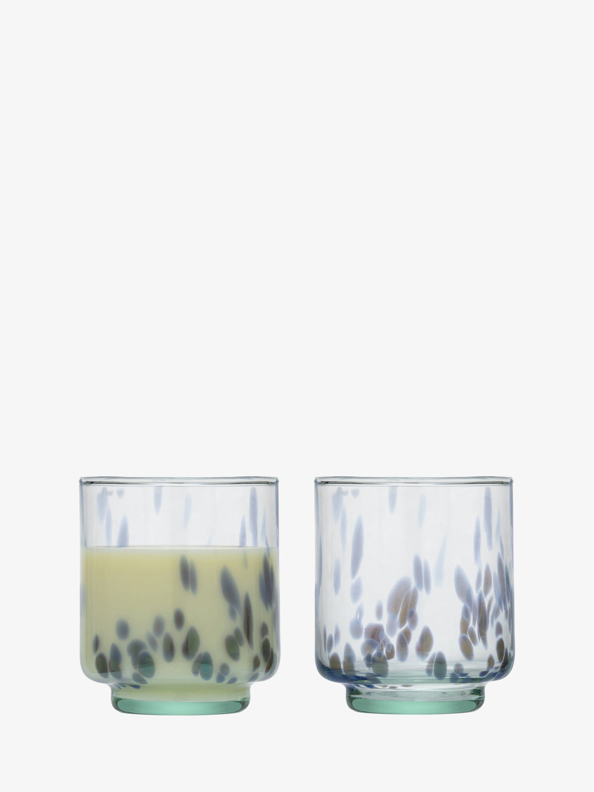 Two lsa-international Tumbler glasses with rounded bases and a clear speckled design featuring scattered black spots. One glass is filled with a pale yellow liquid, while the other remains empty. Both tumblers are displayed side by side against a white background.