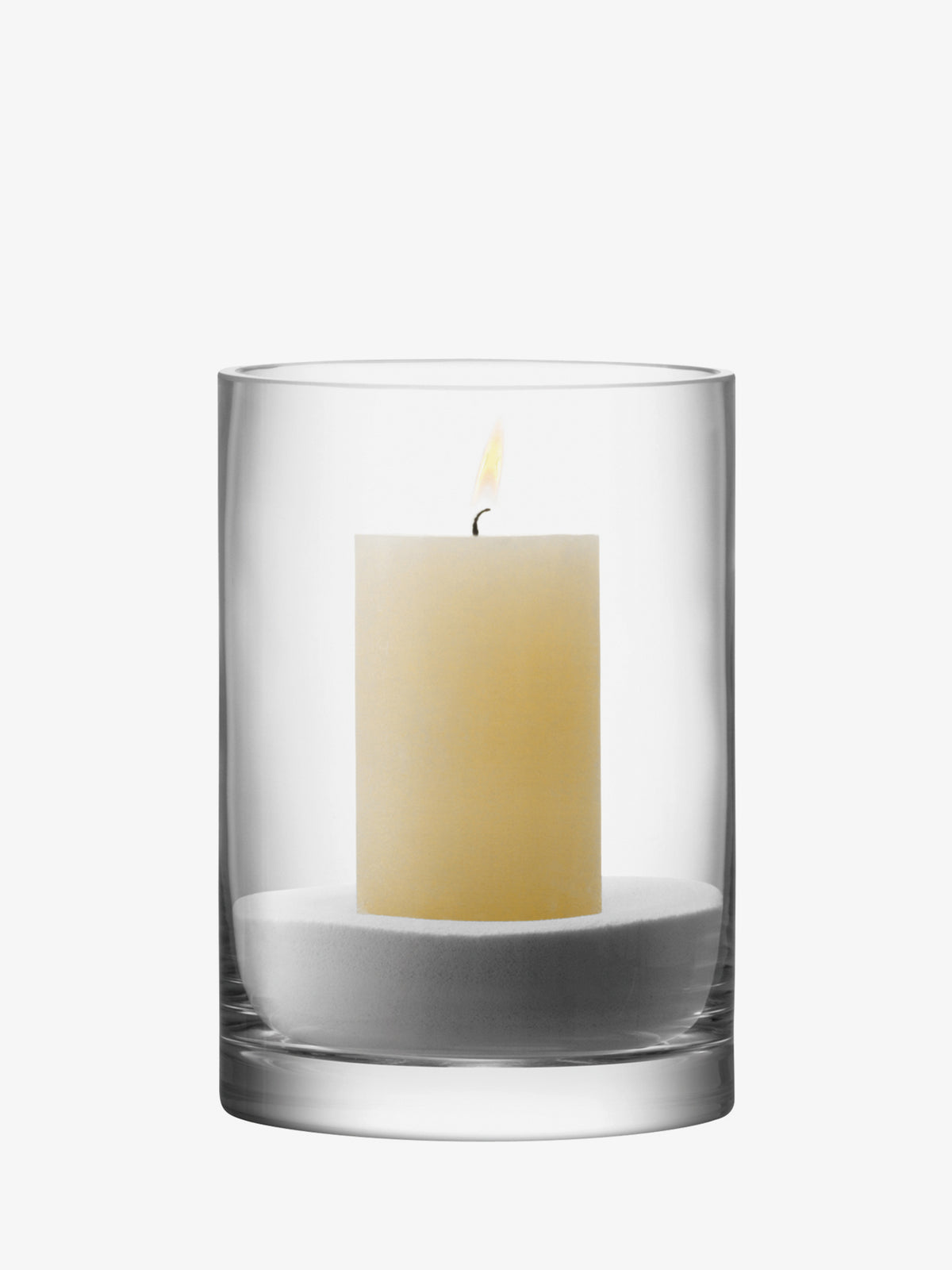 A lit pillar candle sits inside an LSA International Vase/Candleholder, which is a mouth-blown glass lantern filled with white sand.