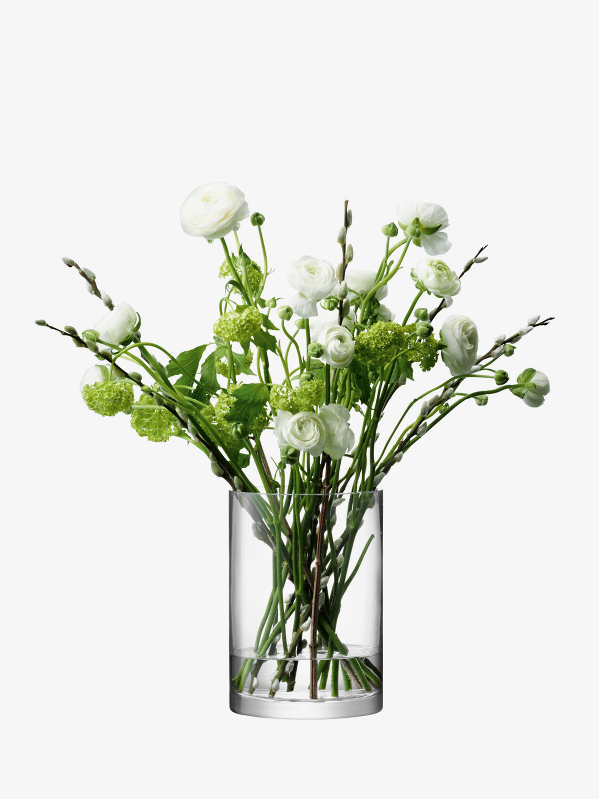 An LSA International Vase/Candleholder made of clear, mouth-blown glass, filled with white ranunculus flowers, green viburnum, and pussy willow stems.