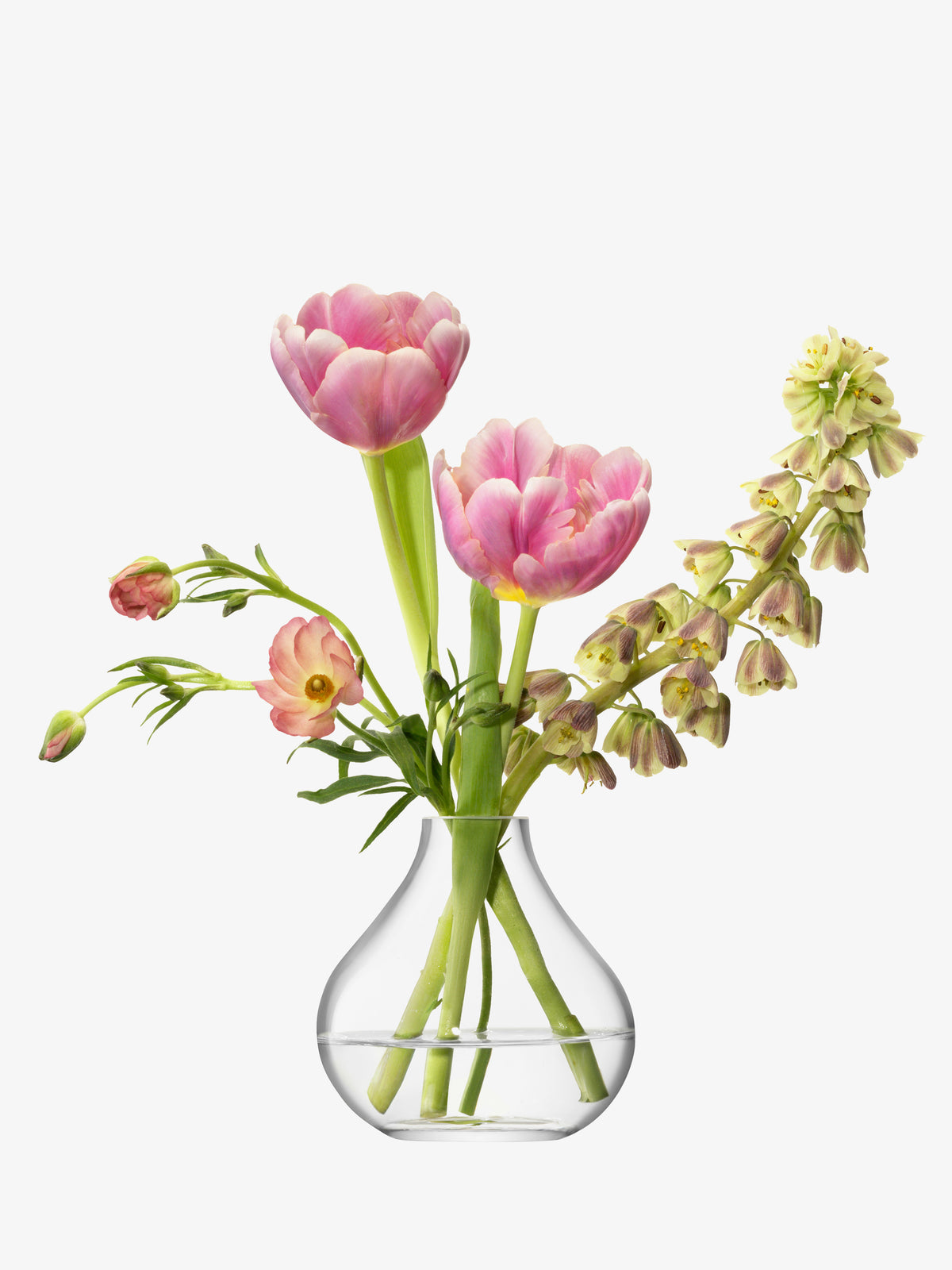 The Sprig Vase by lsa-international, a small mouth-blown glass bud vase, holds pink tulips and other light pink and pale yellow flowers, elegantly displayed against a plain white background.