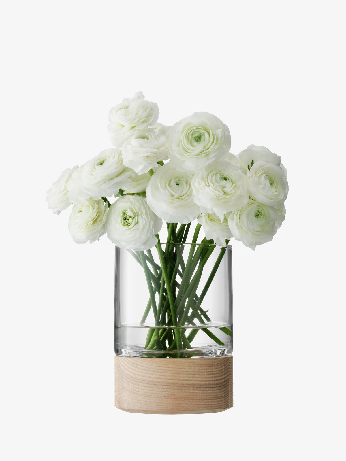 A Vase/Lantern by lsa-international, featuring a clear glass vessel with an ash base, displays several white ranunculus flowers with green stems, arranged against a plain white background.