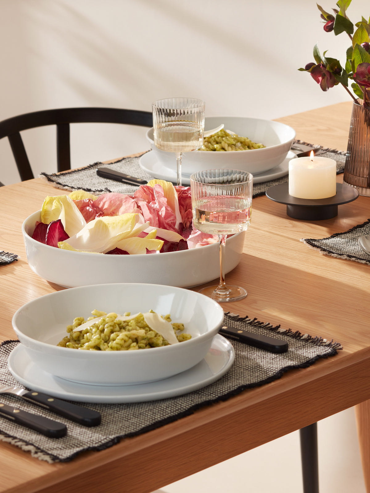 A contemporary, dishwasher-safe LSA International Pasta/Serving Bowl filled with radicchio and endive leaves sits on a wooden dining table between two place settings with bowls of green pasta.