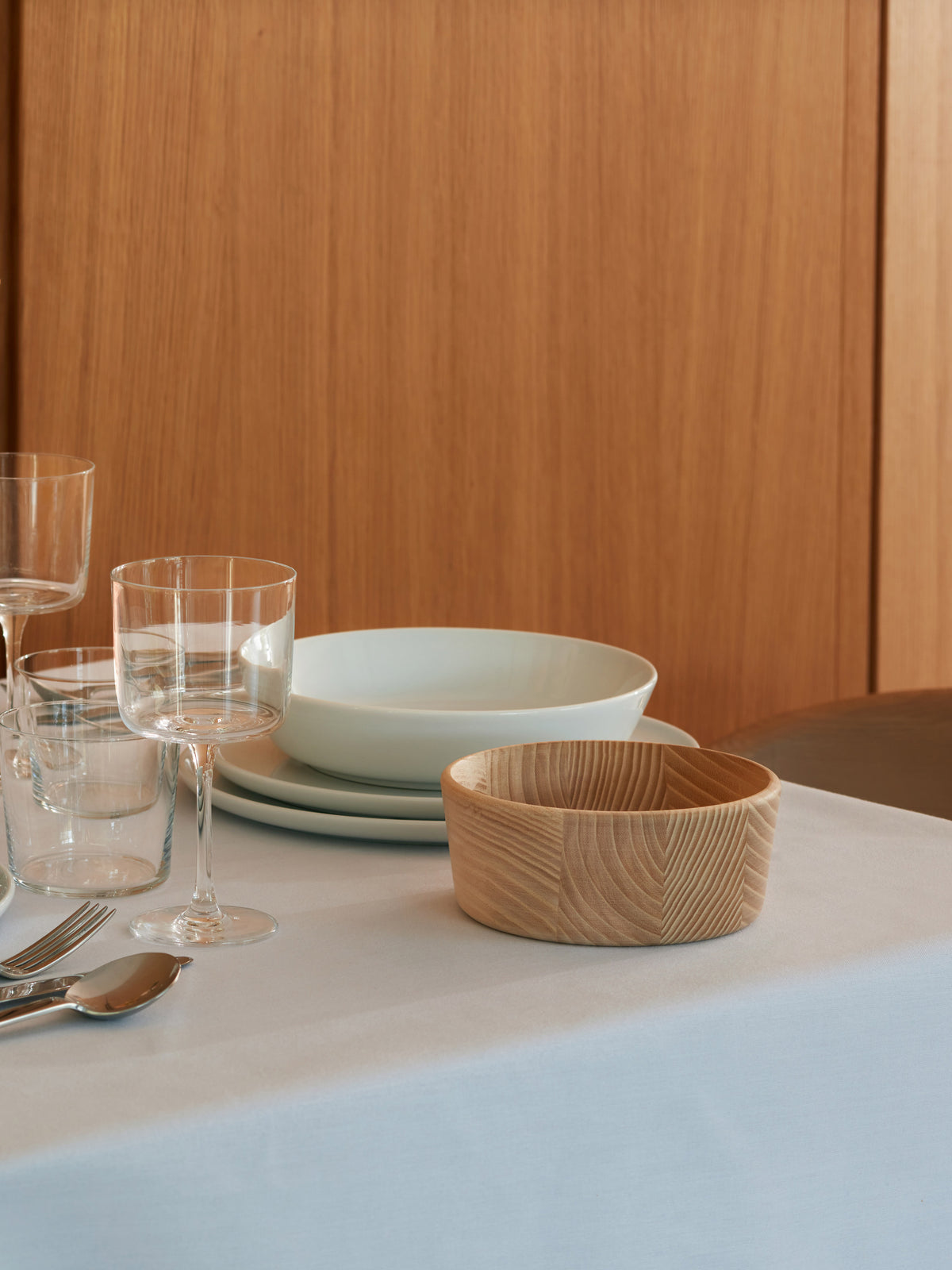 An LSA International Ash Wood Bowl sits on a set table with glassware, plates, and cutlery.