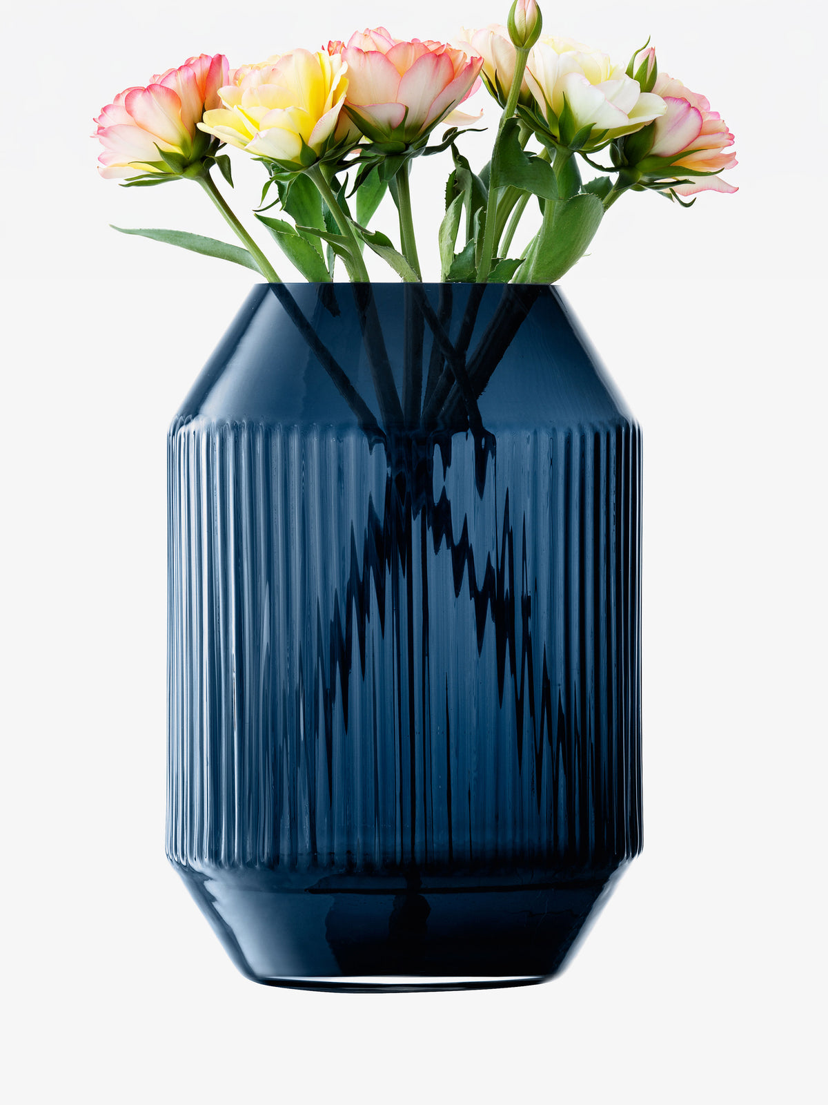 A bouquet of pink and yellow ranunculus flowers in a tall, ribbed sapphire blue lsa-international Lantern/Vase.