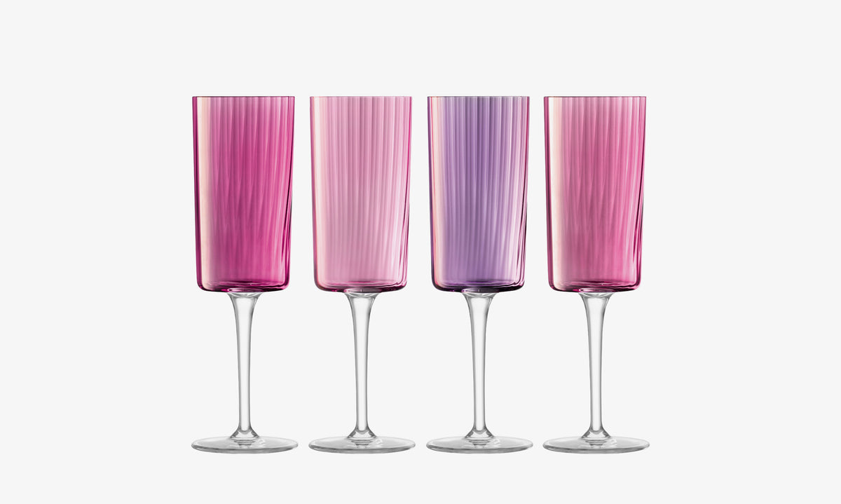 Four tall, textured Champagne Flutes by lsa-international with clear stems are arranged side by side. Their glass features an ombre effect that transitions from pink on the left to purple in the center and returns to pink on the right, creating a striking display reminiscent of hand-painted artistry.