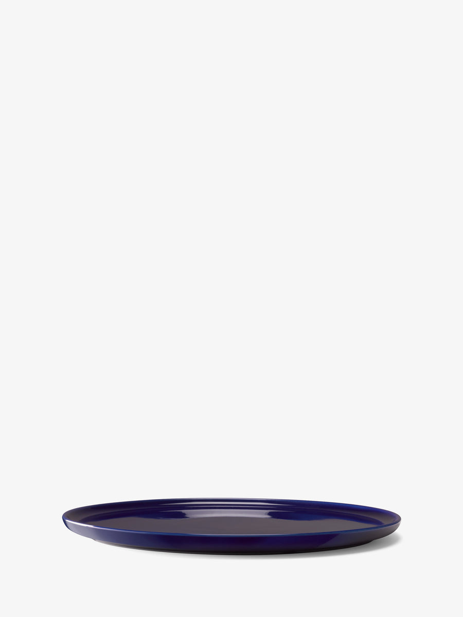 A Dinner Plate by lsa-international is centered on a plain white background. This dark blue, round ceramic plate is seen from a side angle, showcasing its glossy finish and thin, flat shape—a striking example of contemporary tableware designed to elevate any dining experience.